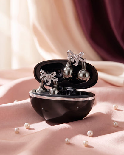Nacary clip-on earbuds in Onyx with crystal bow charms in the open charging case